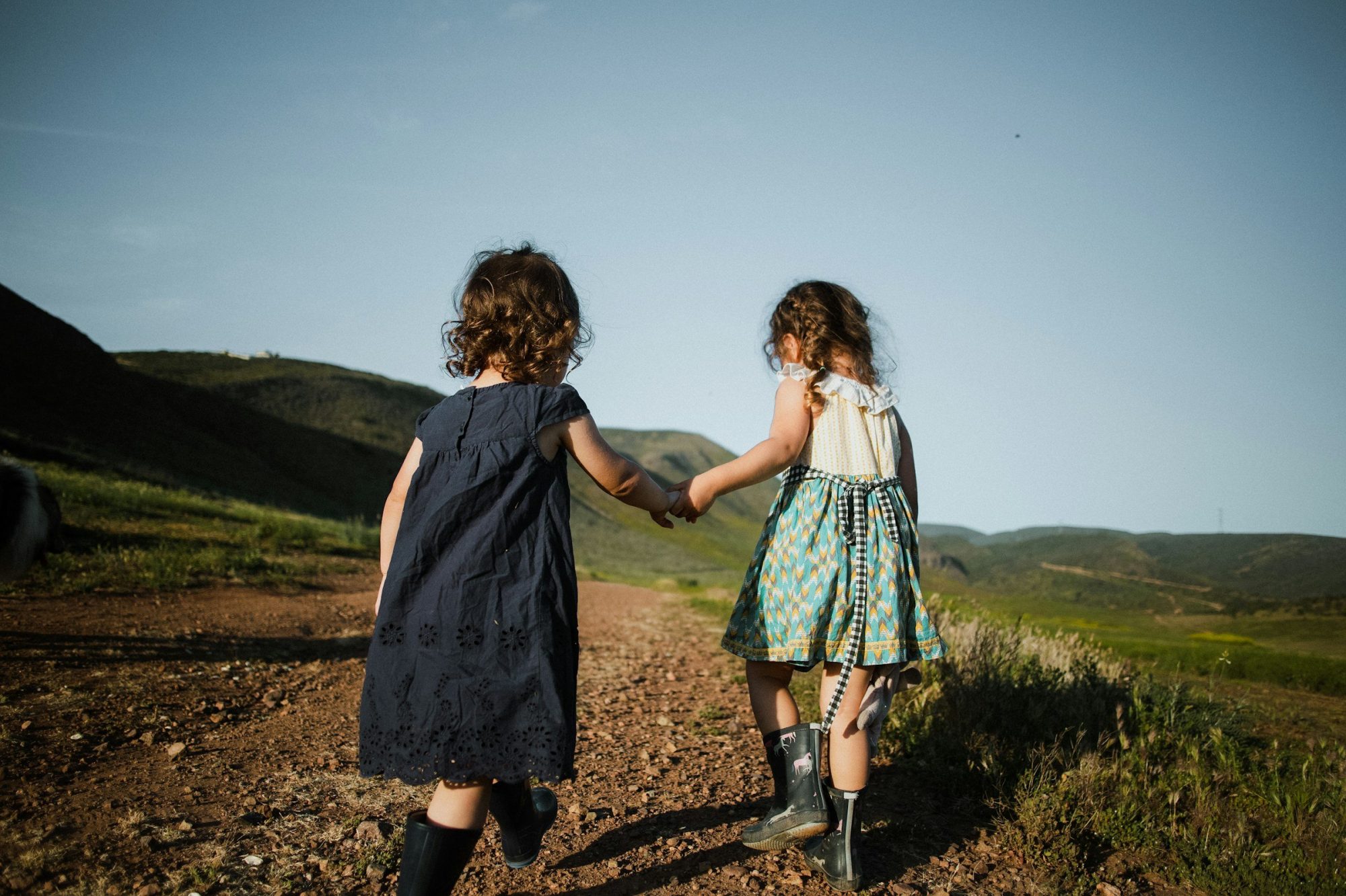 Due bambine, viste di spalle, camminano mano nella mano su un sentiero di campagna.