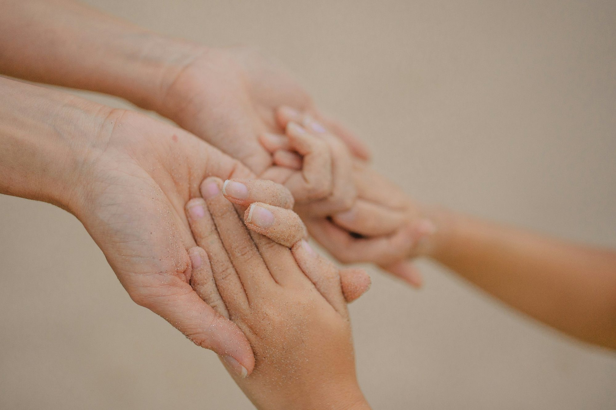 La mano di un adulto accoglie con delicatezza quella di un bambino, su uno sfondo chiaro.