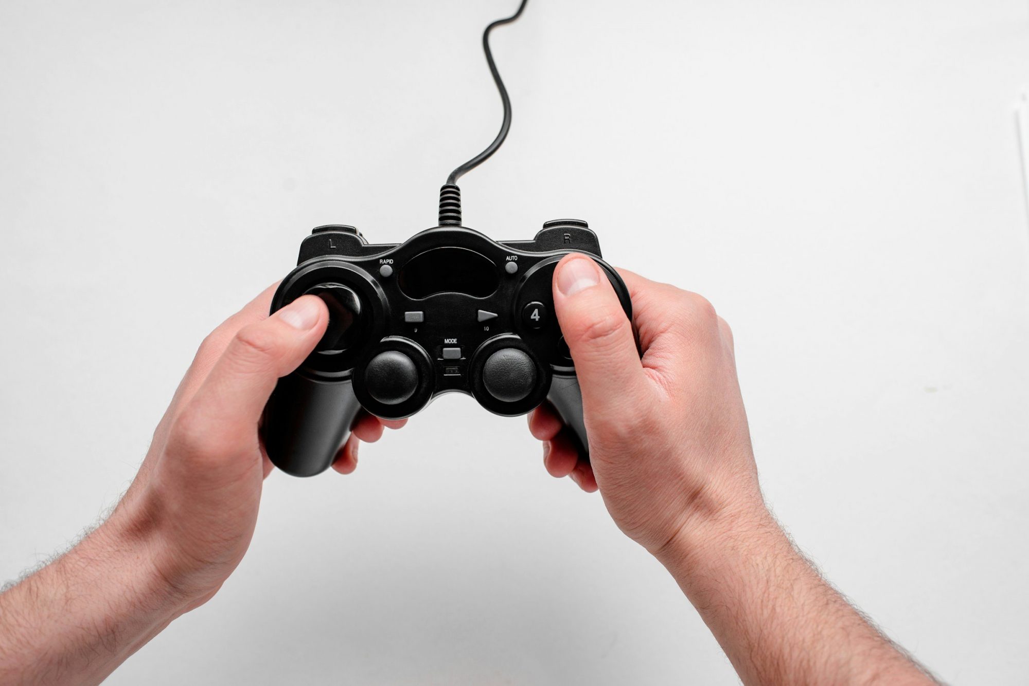 Due mani tengono un controller da videogioco nero con il cavo, su uno sfondo chiaro