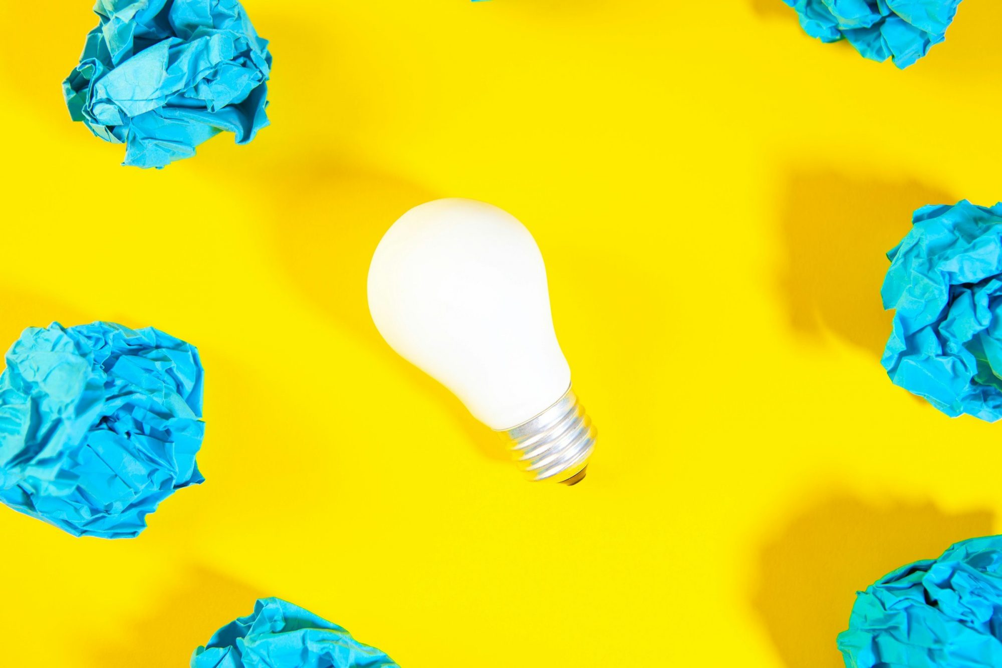 Una lampadina bianca su uno sfondo giallo, circondata da fogli azzurri accartocciati