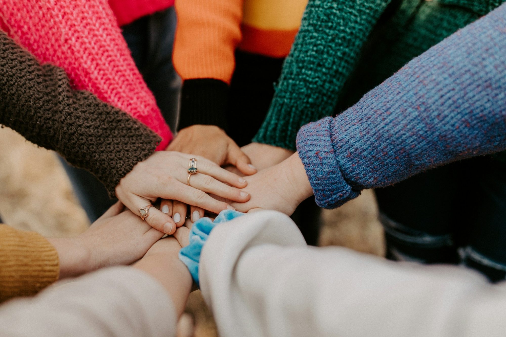 Le mani di più persone si uniscono al centro, una sopra l'altra, in segno di collaborazione.