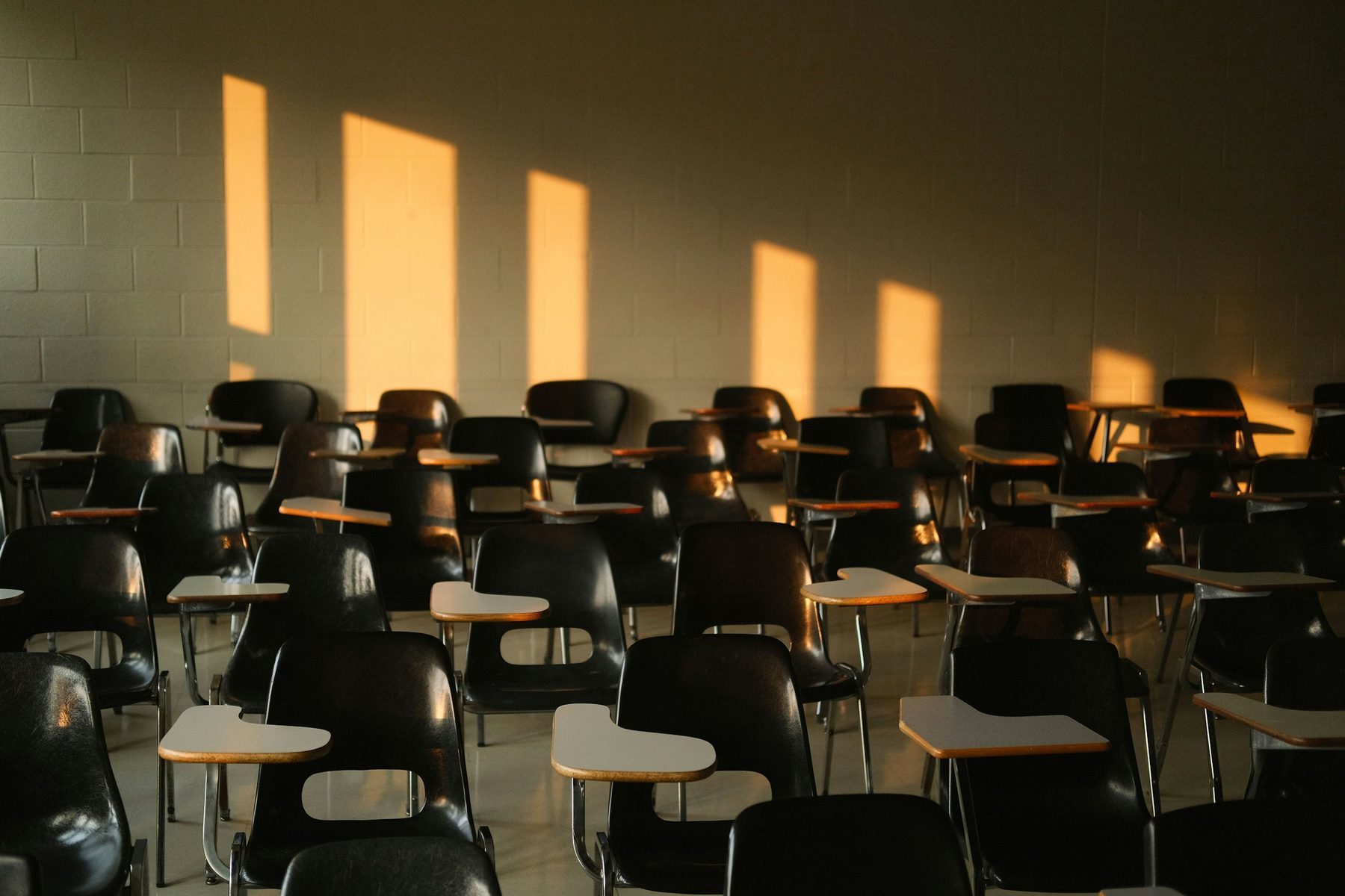 Aula vuota con file di banchi e sedie, attraversata dalla luce calda del pomeriggio