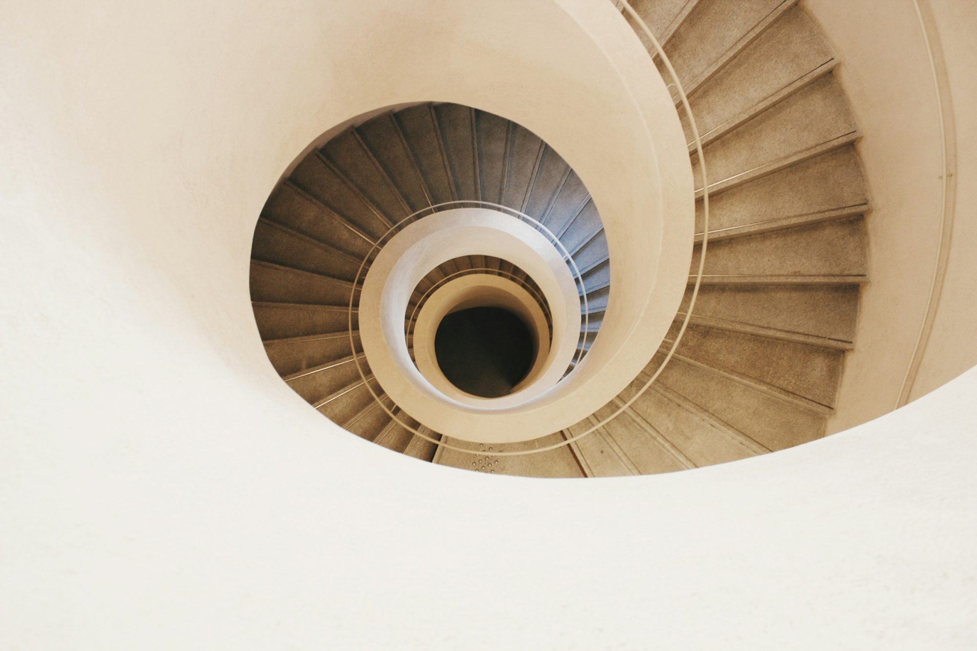 Una scala a chiocciola chiara vista dall'alto, con i gradini che scendono a spirale