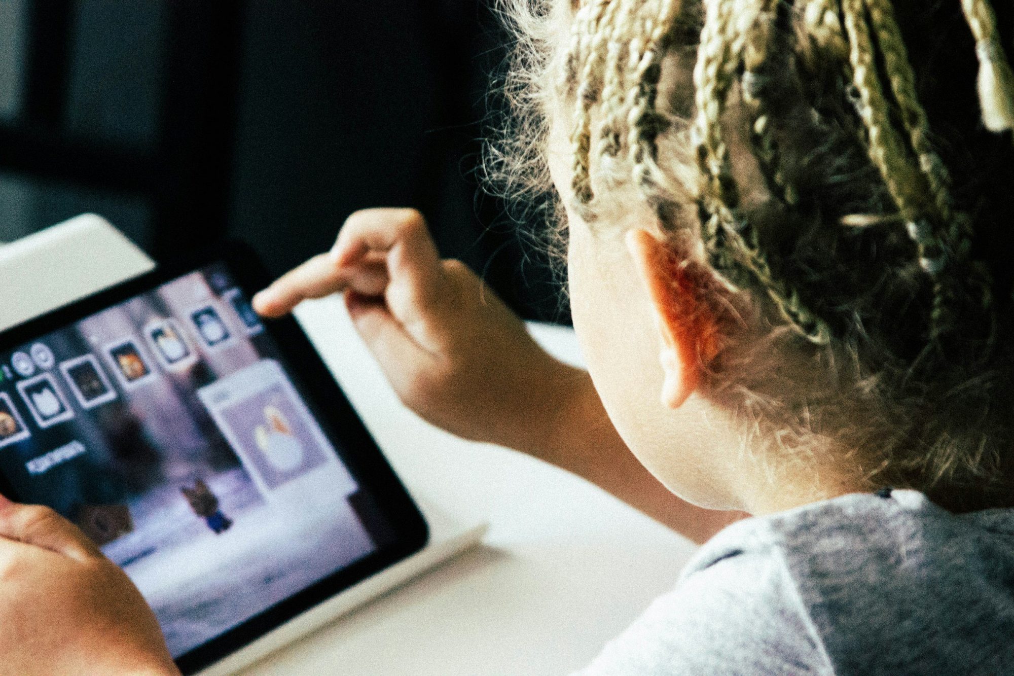 Una bambina vista di spalle tocca lo schermo di un tablet appoggiato su un tavolo.