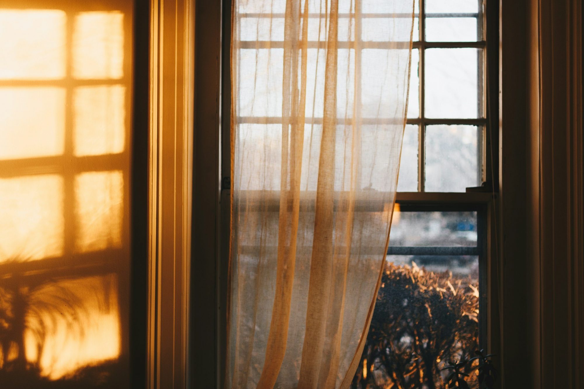 Una tenda leggera davanti a una finestra, attraversata dalla luce dorata del tramonto