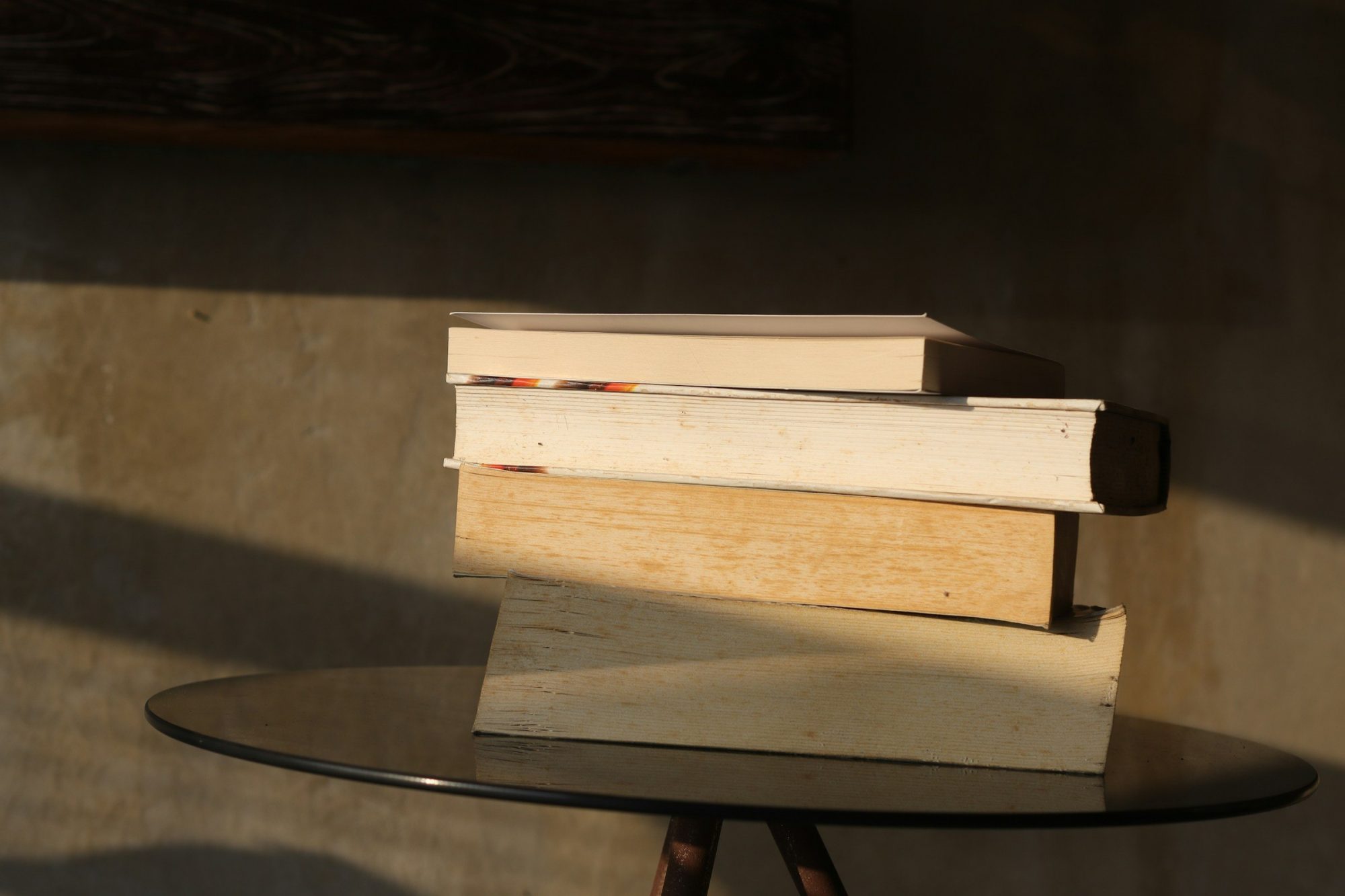 Una pila di libri e fascicoli senza scritte su un tavolino rotondo, illuminata da una lama di luce calda.
