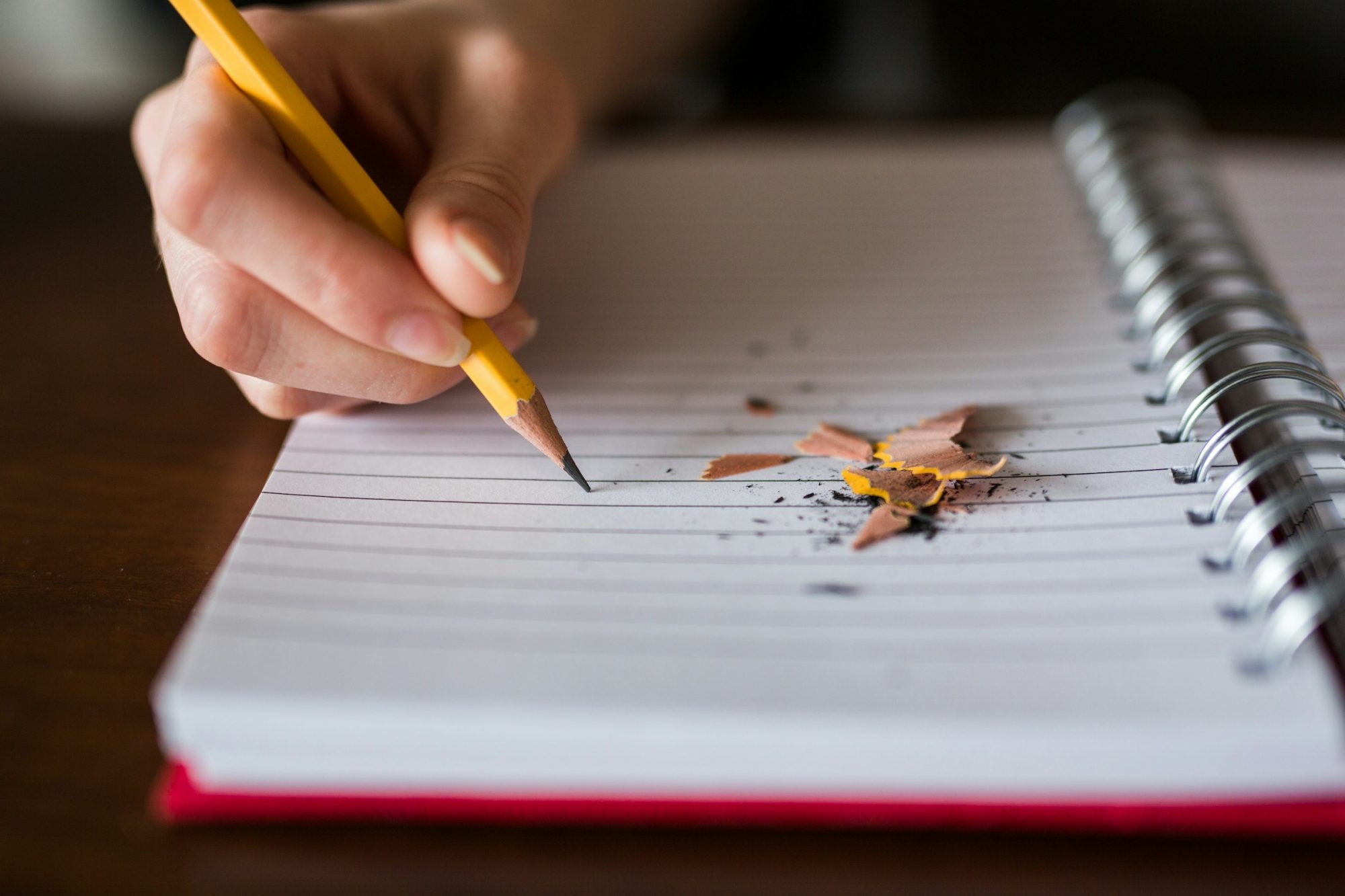 Una mano scrive con la matita su un quaderno a righe, accanto ai trucioli del temperino.