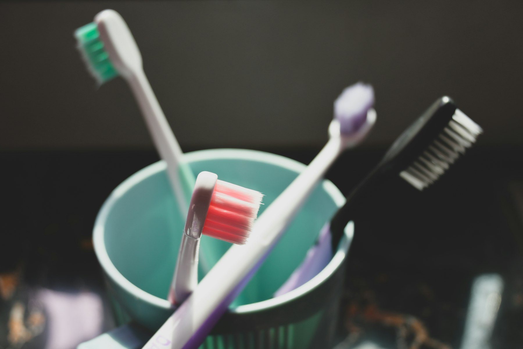 Quattro spazzolini da denti colorati in un bicchiere azzurro, su uno sfondo scuro.