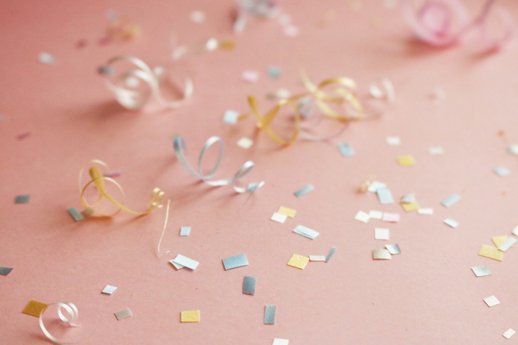 Coriandoli e stelle filanti colorate sparsi su un fondo rosa.
