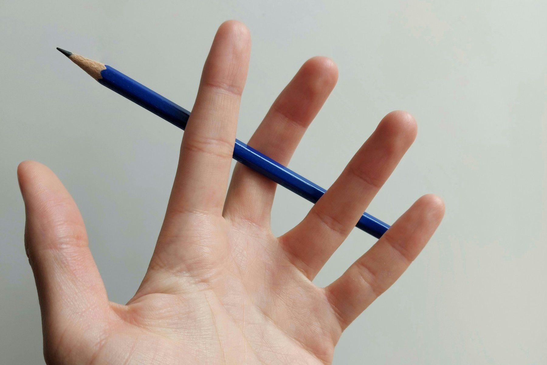 Una mano aperta che tiene una matita blu tra le dita, su sfondo chiaro
