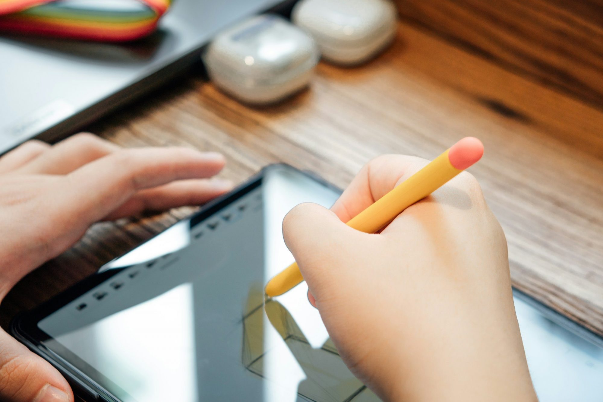 La mano di un bambino disegna con una penna gialla su un tablet, su un tavolo di legno.