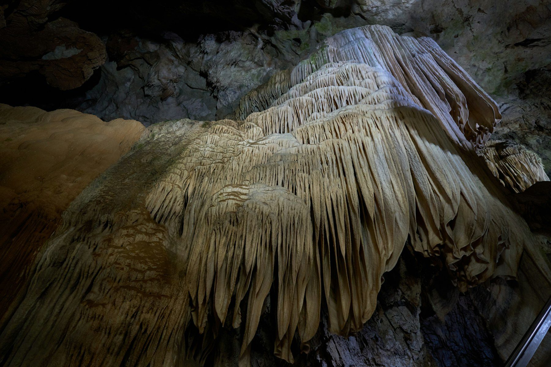 Grandi stalattiti che scendono dal soffitto di una grotta illuminata.