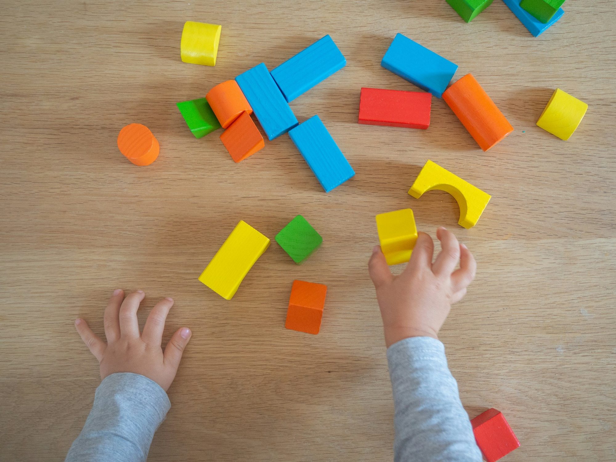 Le mani di un bambino giocano con mattoncini di legno colorati sparsi sul pavimento.