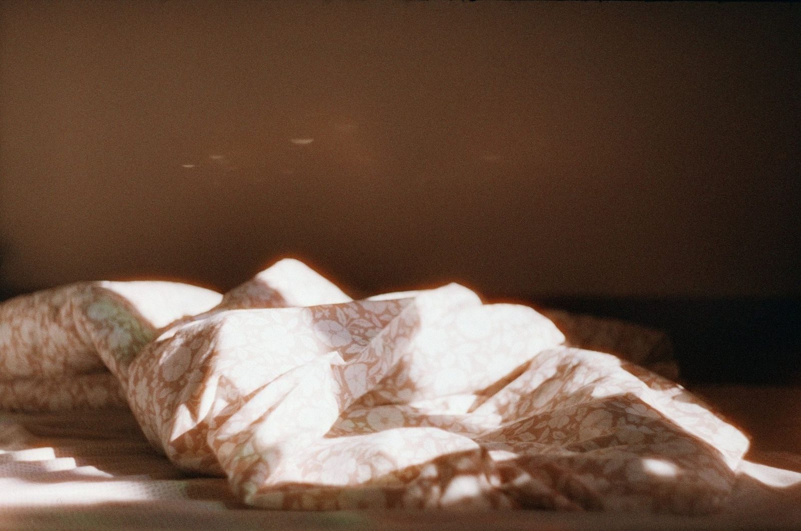 Lenzuola e cuscino stropicciati su un letto, sfiorati da una lama di luce calda