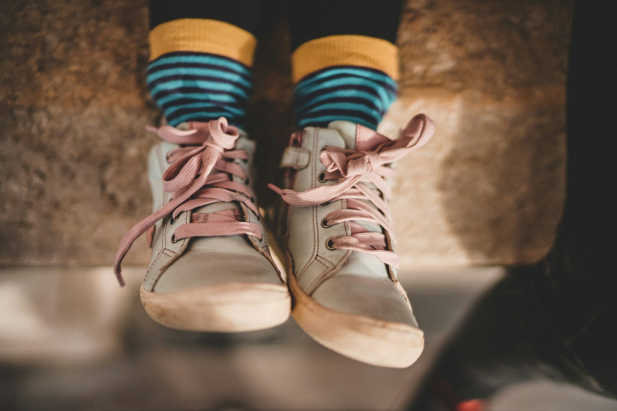 Due piedi con calzini a righe e scarpe di tela chiare, con i lacci rosa allentati.