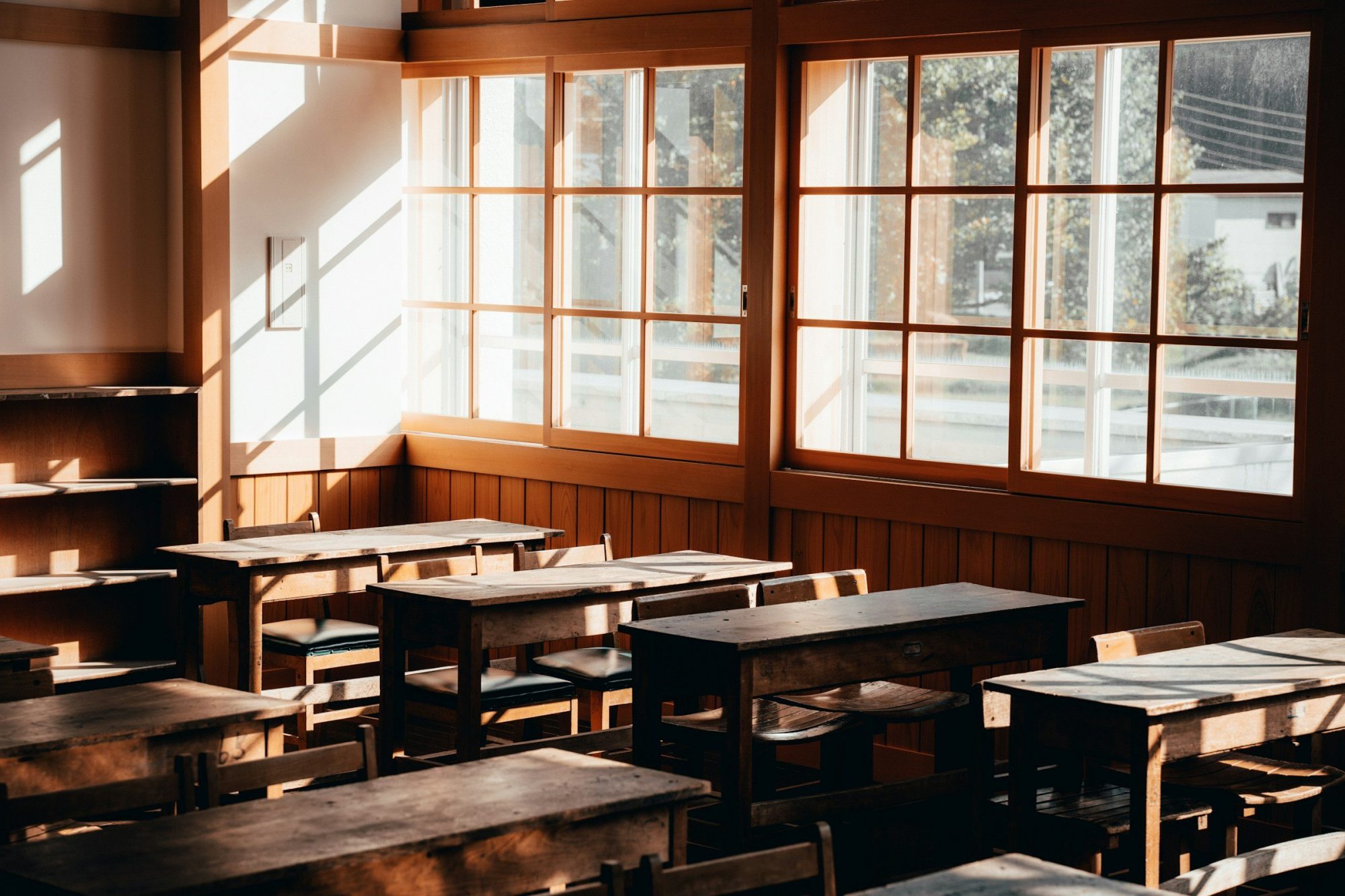 Un'aula vuota con banchi di legno, illuminata dalla luce che entra dalle grandi finestre.